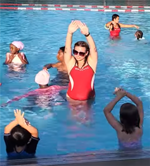 Female lifeguard with hands up showing swimming students how to glide through water